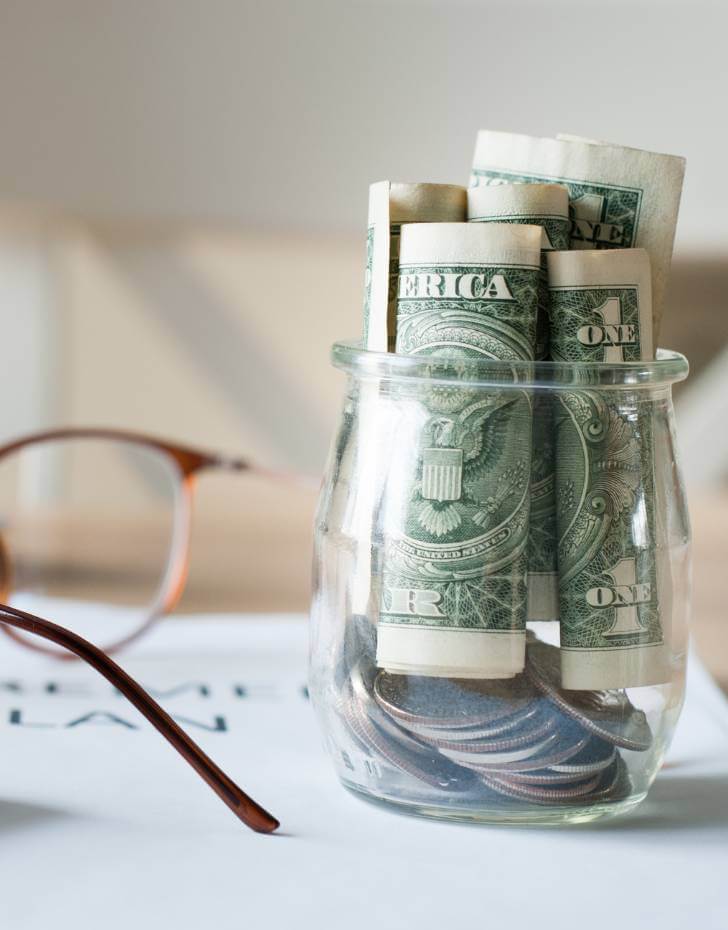 Photo of a stemless wine glass full of money and a pair of reading glasses on top of a retirement plan which includes information about annuities.